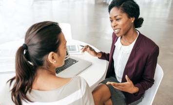 2 women talking and sharing a laptop