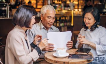 Three people sitting at small table with papers and tablets