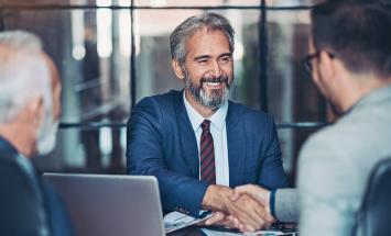 Two men shaking hands over a table with laptop on it