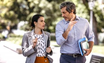 Two people walking and talking with notebooks under their arms