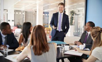 Person standing in front of a table of five people in business suits