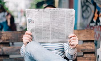 Person sitting on bench reading newspaper