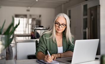 Woman sitting at her laptop while writing in a notebook