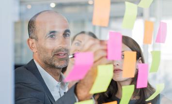 person putting sticky notes on a clear board