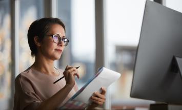 woman with glasses taking notes on a webinar