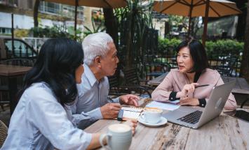 three people at an outdoor table working around a laptop