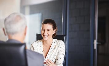 Person at desk talking to a white haired person