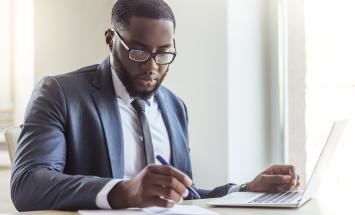 Person wearing a suit reviewing documents in front of a computer