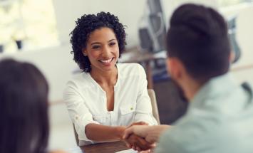 Woman sitting and smiling while shaking hands across table.