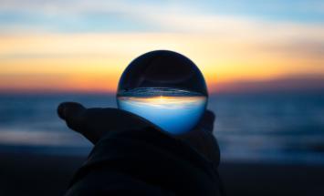 person holding glass orb reflecting the horizon
