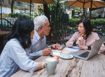 Three people at a table with a laptop and papers