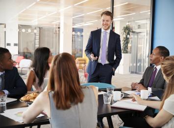 Person standing in front of a table of five people in business suits