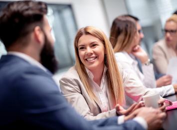People sitting at a conference table and one of them is smiling at the camera