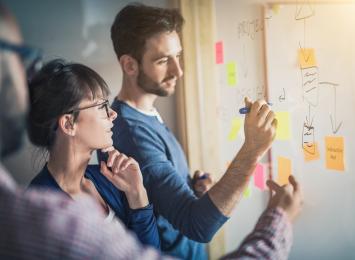 people drawing on a white board with sticky notes