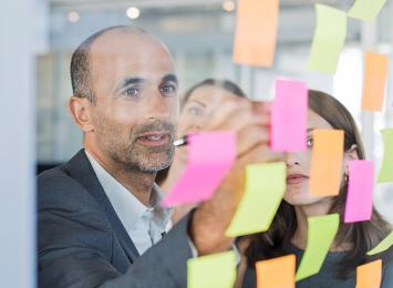 person putting sticky notes on a clear board