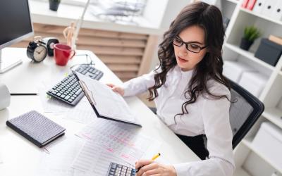 Person with long hair working at a desk with a calculator and computer