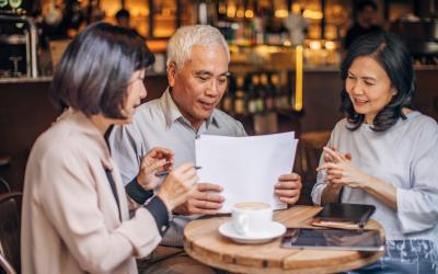 Three people sitting at small table with papers and tablets