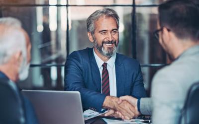 Two men shaking hands over a table with laptop on it