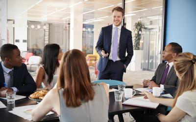 Person standing in front of a table of five people in business suits