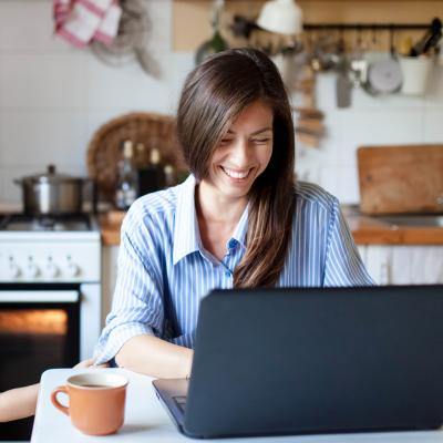 Person with a child in the kitchen on a laptop smiling 